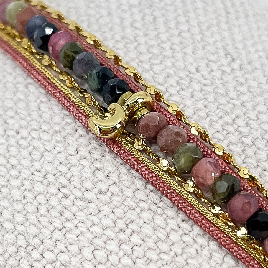 Bracelet composés de plusieurs liens cordons et chaine doré et rose s'enroulant autour du poignet. Sur un cordon des perles de pierre naturelle de tourmalines multicolores sont ponctuées par un pendentif croissant de lune doré.
