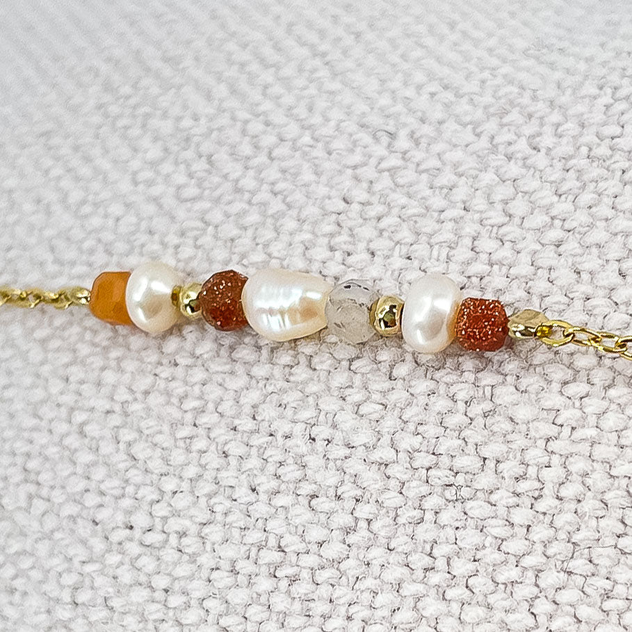 Bracelet monté avec une alternance de perles de culture et de pierres de lune naturelles et perle de verre pailletée de teinte terracotta sur une chaîne dorée.