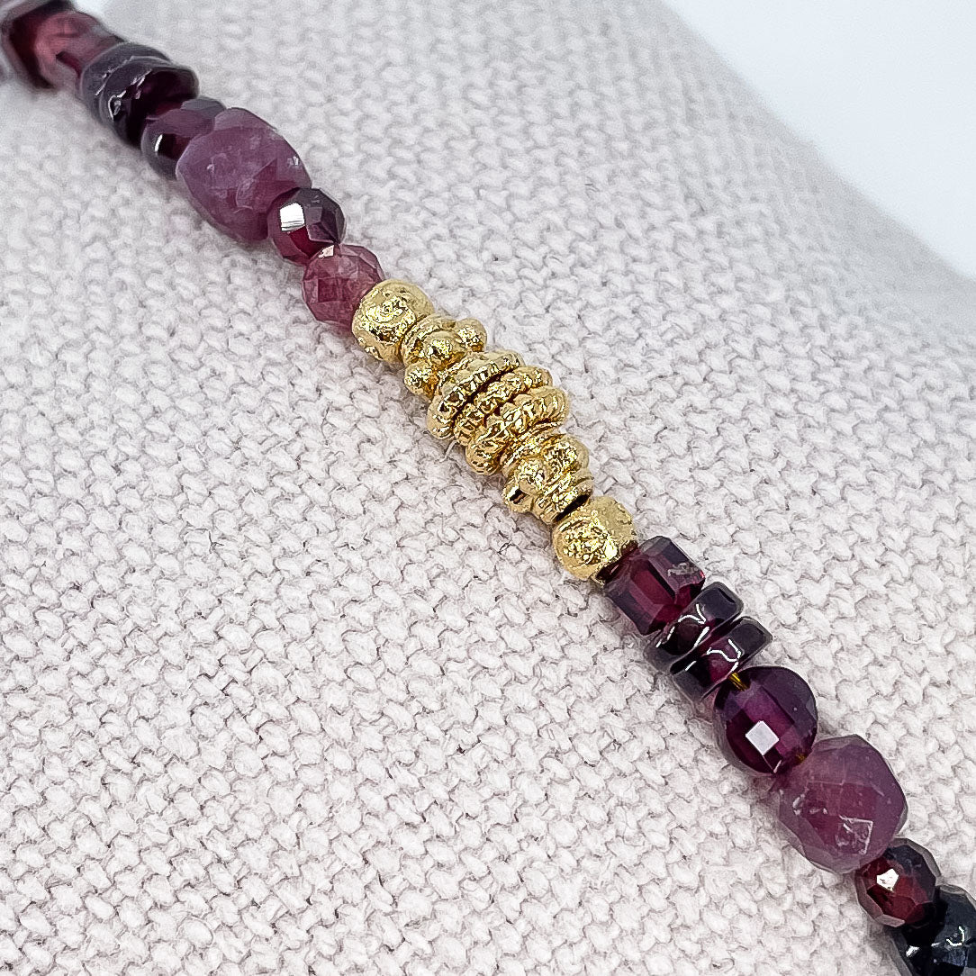 Bracelet pierres naturelles Tourmaline et Grenat dans une déclinaison de teintes bordeaux-rose profond. Perles dorées multiformes au centre du bracelet.