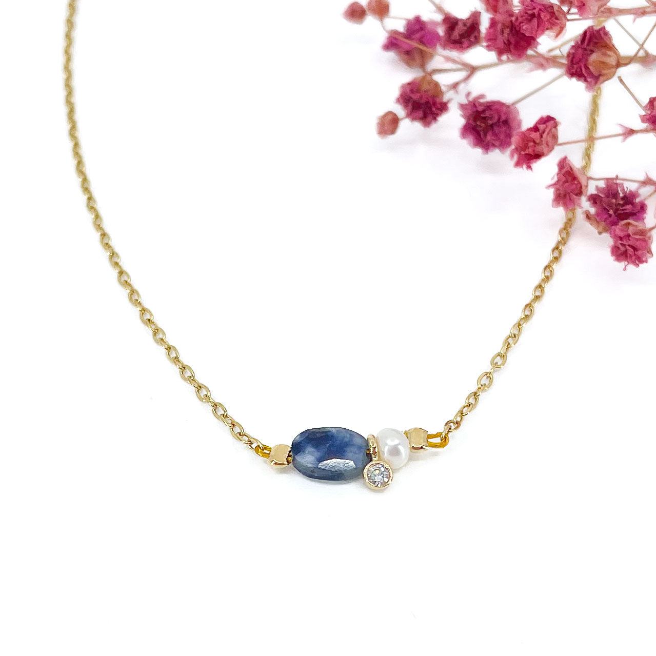 Collier en pierre fine naturelle Saphir Bleu orné d'une perle de culture et d'un petit pendentif cristal éclatant. Monté sur chaîne dorée en acier inoxydable.