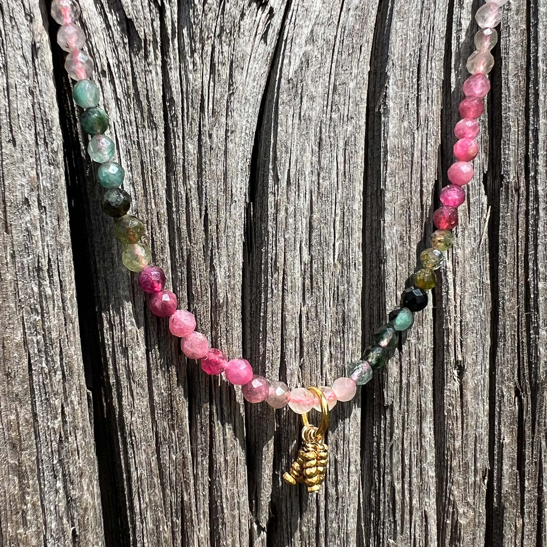 Collier rivière de perles de pierres fines naturelles de Tourmaline teinte arc-en-ciel. Pendentif composé de petites pierres d'hématite dorée. Chaîne de fermeture ajustable de 39 à 44 cm.